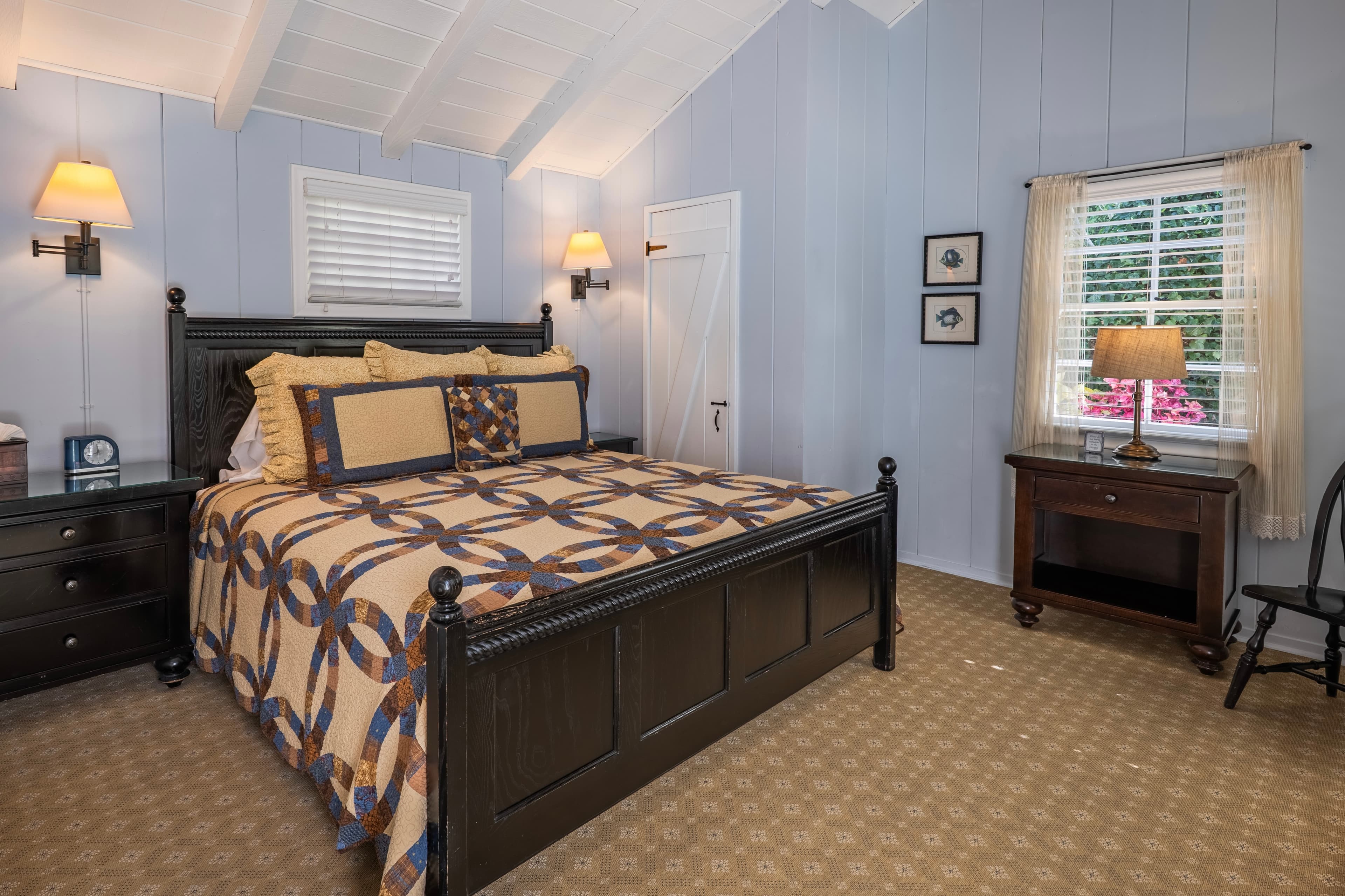 A cozy bedroom in a cottage with a vaulted ceiling, featuring a large dark wood bed frame, light blue walls, and a warm patterned quilt.